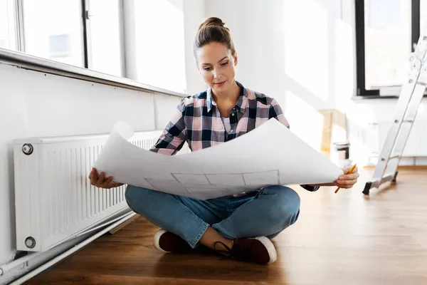 Woman with blueprint sitting on floor at home — Stock Photo, Image