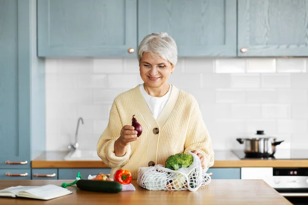 Mujer con verduras y libro de cocina en la cocina — Foto de Stock