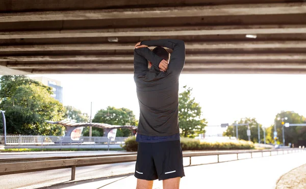 Man stretching shoulder under bridge — Stock Photo, Image