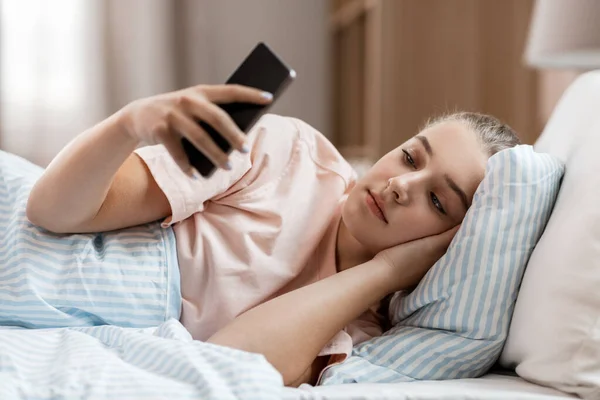 Dívka s chytrým telefonem v posteli doma — Stock fotografie