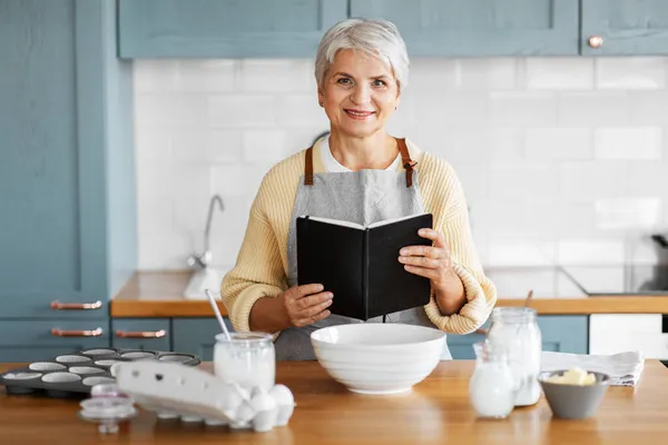 Щаслива жінка з кулінарною книгою готує їжу на кухні — стокове фото