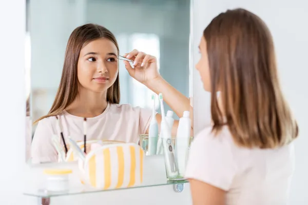Teenage girl tweezing her eyebrow at bathroom — Stock Photo, Image