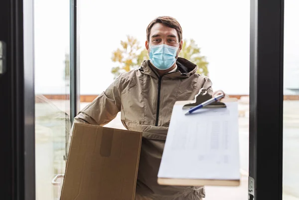 Bezorger in masker met pakketdoos en klembord — Stockfoto