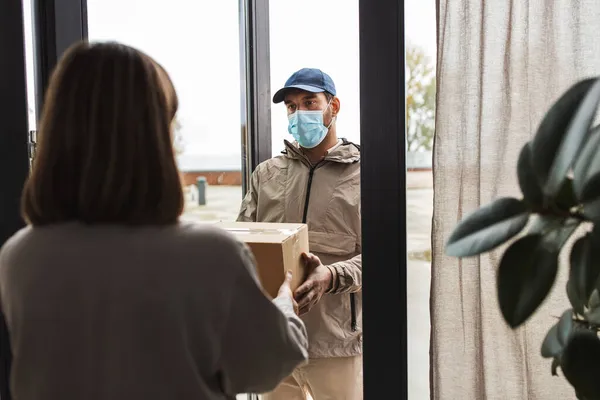 Delivery man in mask giving parcel to customer — Stock Photo, Image