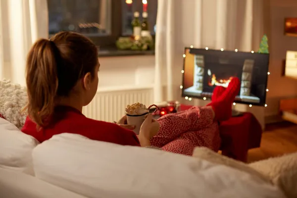 Женщина смотрит телевизор со сливками и зефиром на Рождество — стоковое фото