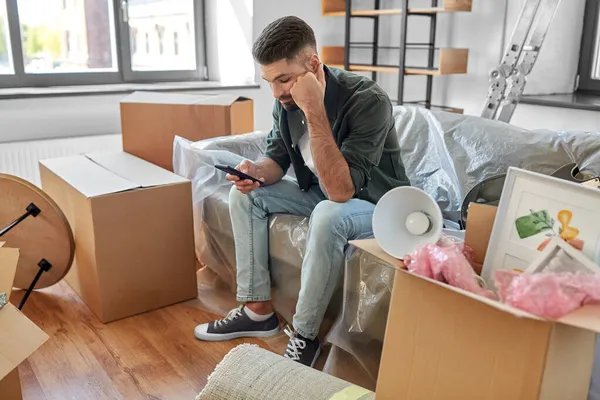 Ledsen man med smartphone och lådor flyttar hem — Stockfoto