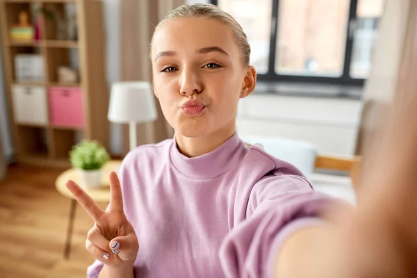 Chica tomando selfie en casa y mostrando paz —  Fotos de Stock