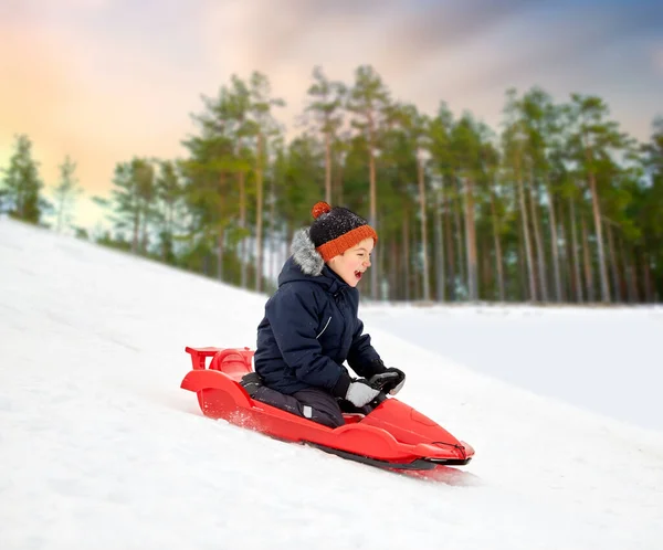 Niño feliz deslizándose en trineo colina abajo de la nieve en invierno —  Fotos de Stock