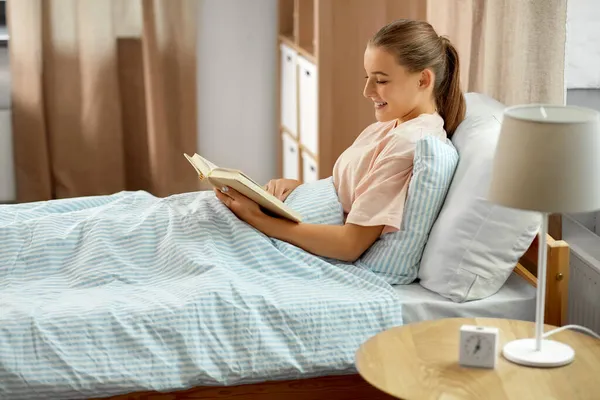 Sorrindo livro de leitura menina na cama em casa — Fotografia de Stock