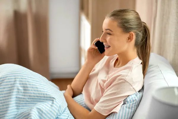 Szczęśliwa dziewczyna ze smartfonem dzwoniącym w łóżku w domu — Zdjęcie stockowe