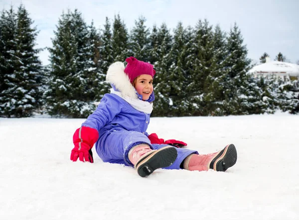 Fröhliches kleines Mädchen in Winterkleidung sitzt auf Schnee — Stockfoto