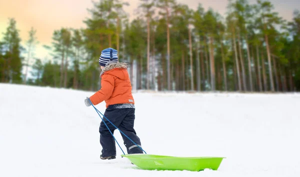 Liten pojke med släde klättring snow hill i vinter — Stockfoto