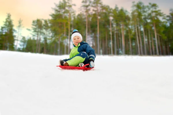 Menino feliz deslizando no trenó colina de neve no inverno — Fotografia de Stock