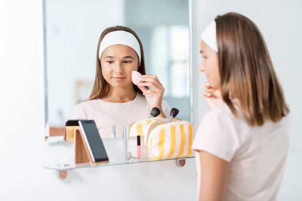 Adolescente con smartphone utilizzando make up spugna — Foto Stock