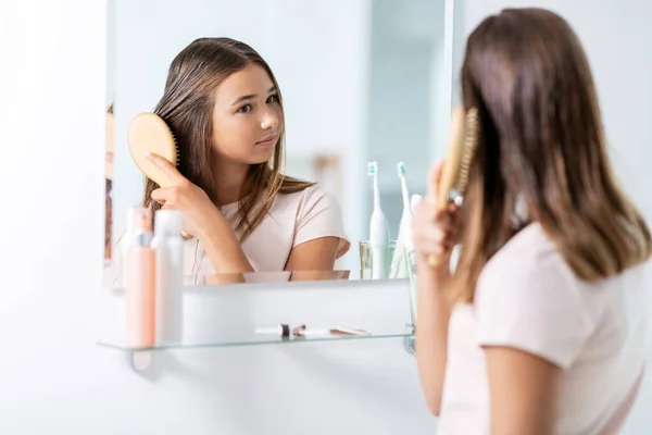 Teenage girl brushing hair with comb at bathroom — Stock Photo, Image