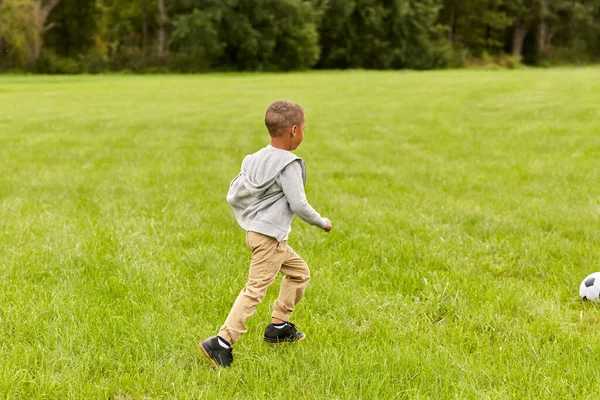 Маленький мальчик с мячом играет в футбол в парке — стоковое фото