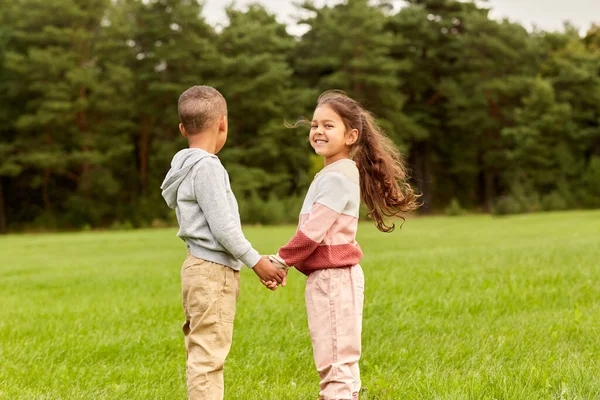 Szczęśliwy mały chłopiec i dziewczyna trzymając się za ręce w parku — Zdjęcie stockowe