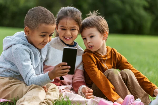 Niños con teléfono inteligente sentado en una manta en el parque —  Fotos de Stock