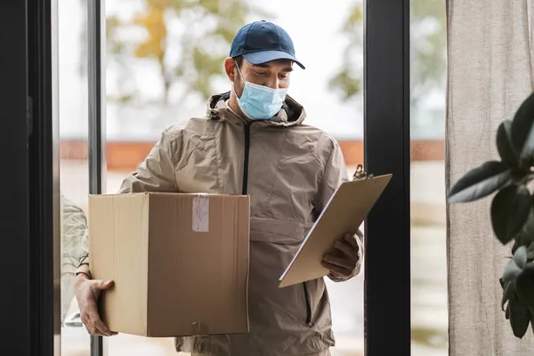 Delivery man in face mask holding parcel box — Stock Photo, Image