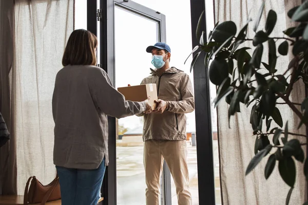 Delivery man in mask giving parcel to customer — Stock Photo, Image
