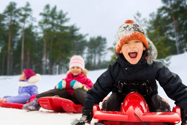 Niños felices deslizándose en trineos en invierno — Foto de Stock