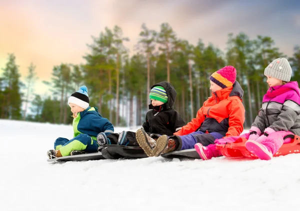 Glückliche kleine Kinder, die im Winter auf Schlitten rutschen — Stockfoto