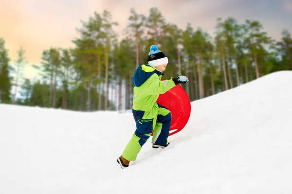 Счастливый мальчик со снежным блюдцем на санях зимой — стоковое фото