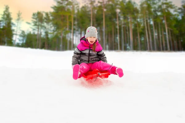 Gelukkig klein meisje glijden naar beneden op slee in de winter — Stockfoto