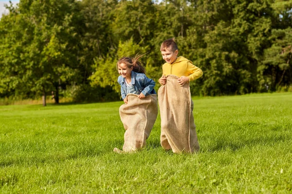 Niños felices jugando juego de saltos bolsa en el parque — Foto de Stock