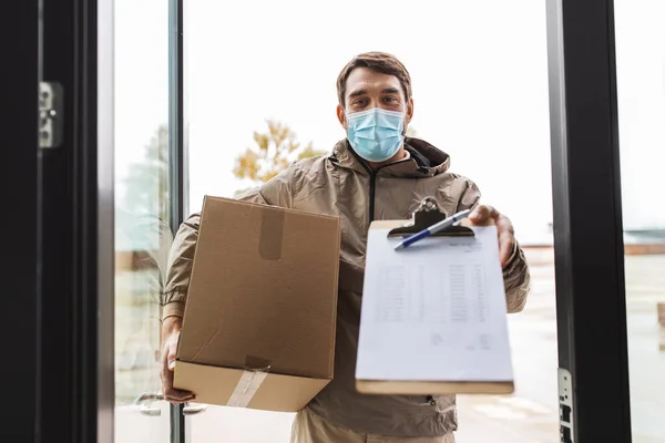 Delivery man in mask with parcel box and clipboard — Stock Photo, Image