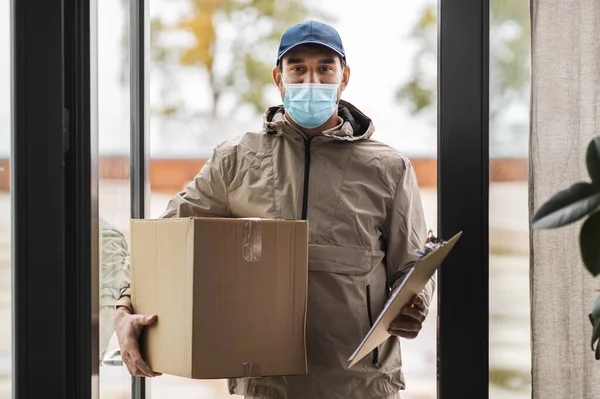 Pria pengiriman dalam masker wajah memegang kotak paket — Stok Foto