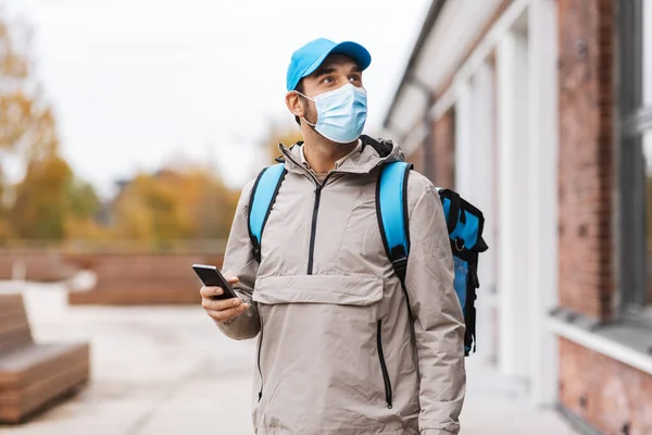Fattorino in maschera con telefono e borsa termica — Foto Stock
