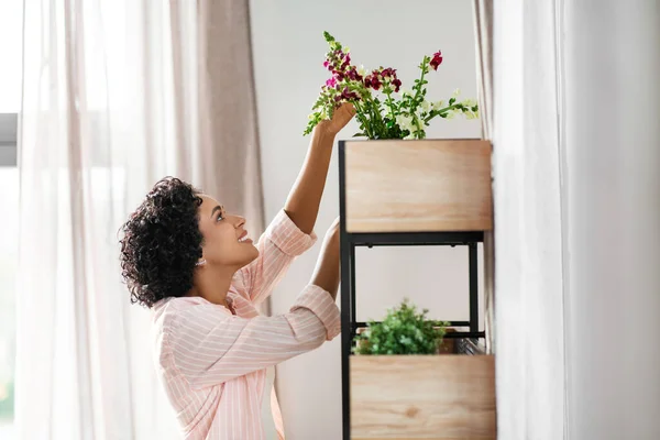 Nő tesz virágokat a polcra otthon — Stock Fotó