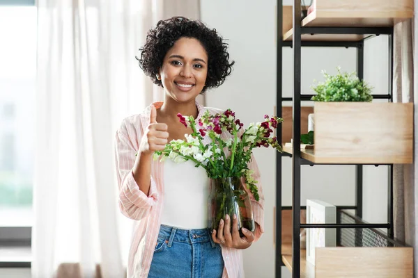 Sonriente mujer sosteniendo flores en jarrón en casa —  Fotos de Stock