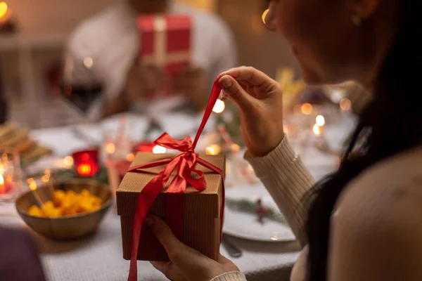 Mujer feliz abriendo regalo de Navidad en la cena —  Fotos de Stock