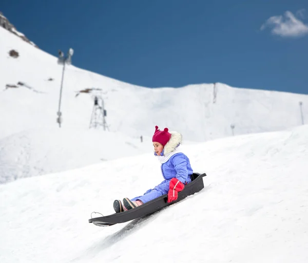 Счастливая маленькая девочка, спускающаяся на санях зимой — стоковое фото