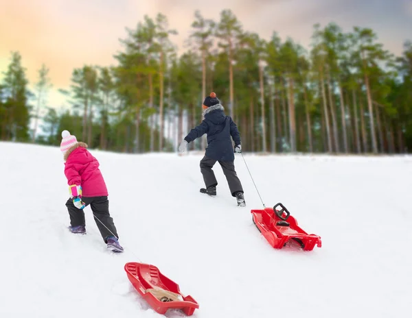Дети с санями зимой карабкаются на снежный холм — стоковое фото
