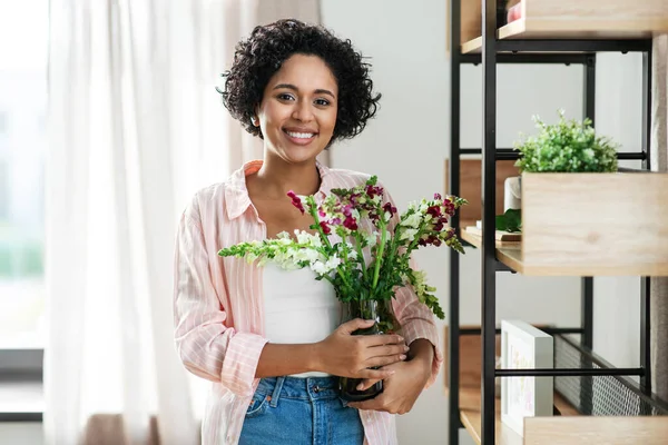 Sonriente mujer sosteniendo flores en jarrón en casa —  Fotos de Stock