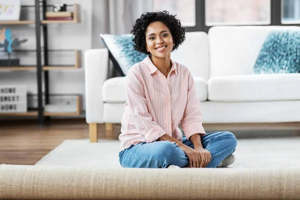 Sorridente giovane donna seduta su tappeto a casa — Foto Stock