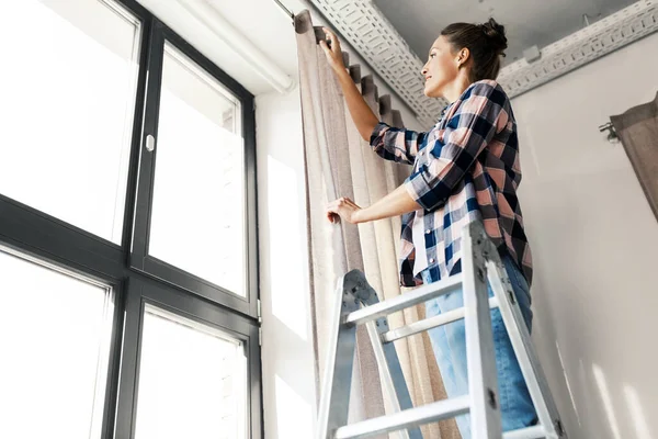 Mujer en escalera colgando cortinas en casa —  Fotos de Stock