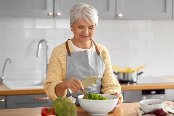 Щаслива жінка додає олію до салату на кухні — стокове фото