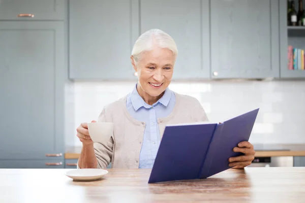 Feliz mulher sorrindo livro de leitura na cozinha — Fotografia de Stock