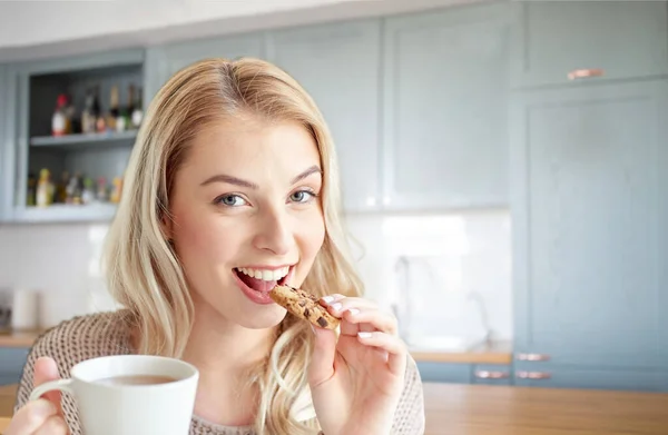 Щаслива жінка з чаєм їсть печиво на кухні — стокове фото