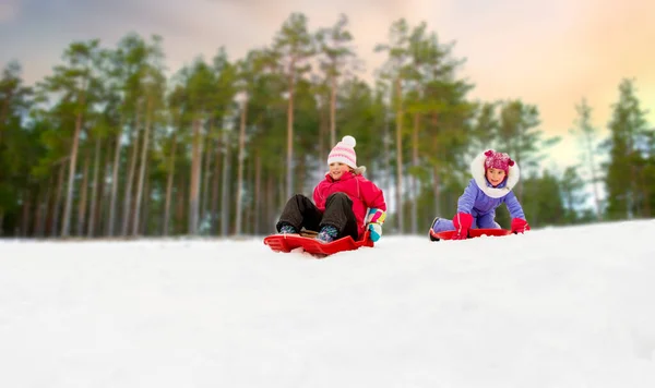 Meisjes glijden op sleeën bergafwaarts sneeuw in de winter — Stockfoto