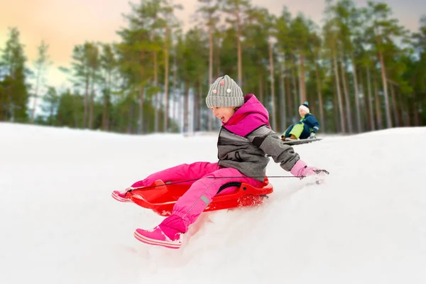 Gelukkig klein meisje glijden naar beneden op slee in de winter — Stockfoto