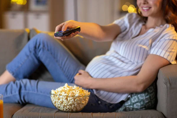 Mujer embarazada con control remoto viendo la televisión —  Fotos de Stock