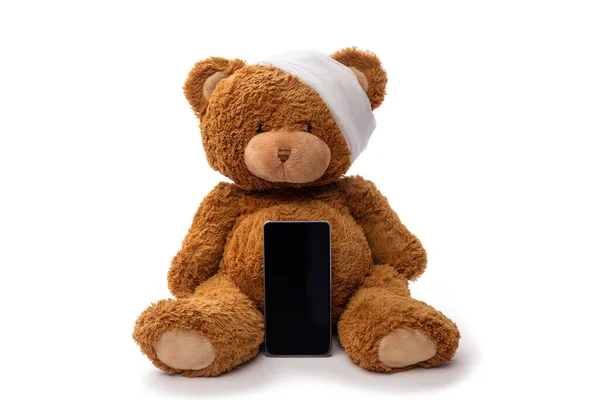 テディベアのおもちゃに包帯された頭とスマートフォン — ストック写真