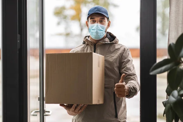 Delivery man in mask with box showing thumbs up — Stock Photo, Image