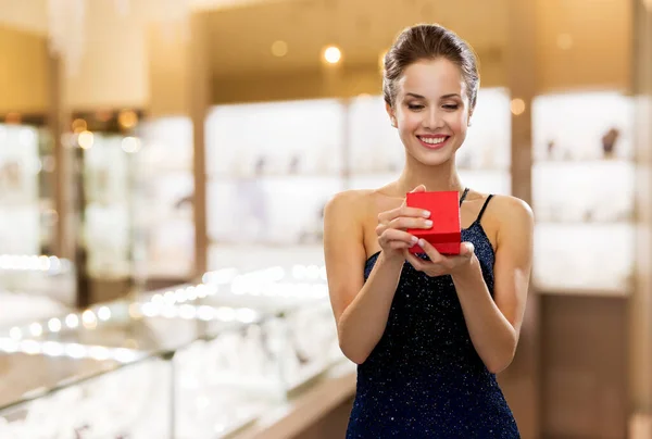 Усміхнена жінка з червоною подарунковою коробкою в магазині ювелірних виробів — стокове фото