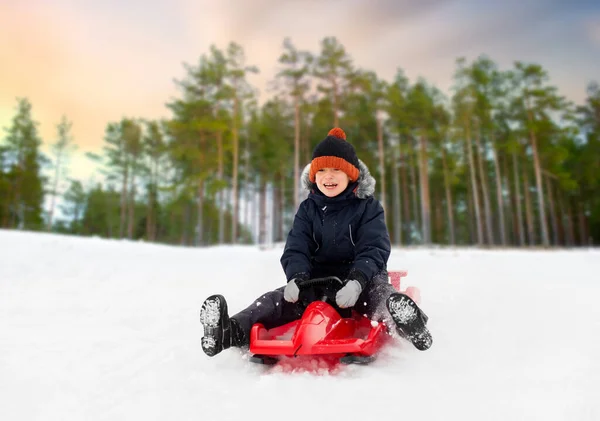 Glücklicher Junge rutscht im Winter auf Schlitten den Schneehügel hinunter — Stockfoto
